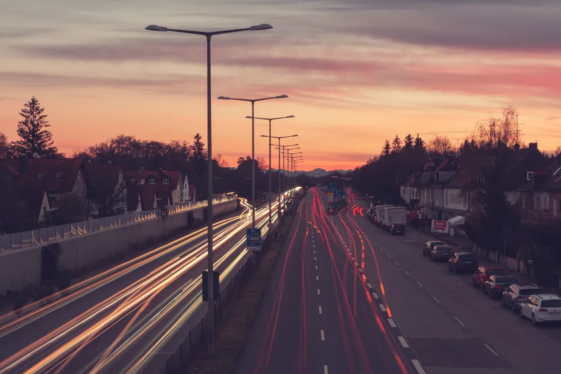 Mehrspurige Ausfallstraße in der Abenddämmerung, rote und weiße Lichtspuren ziehen durch das Bild.